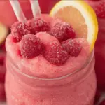 Refreshing frozen raspberry lemonade in a glass, garnished with raspberries and mint on a sunny patio.